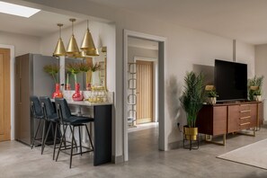 Una cocina moderna con taburetes de bar, luces colgantes y un televisor en la sala de estar.