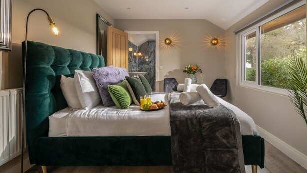 A modern bedroom with a large bed, a bedside table with a fruit bowl, and a view of greenery through the window. - Clarence Estate - Eight Bedroom Villa, Sleeps 20 (Woodnesborough)