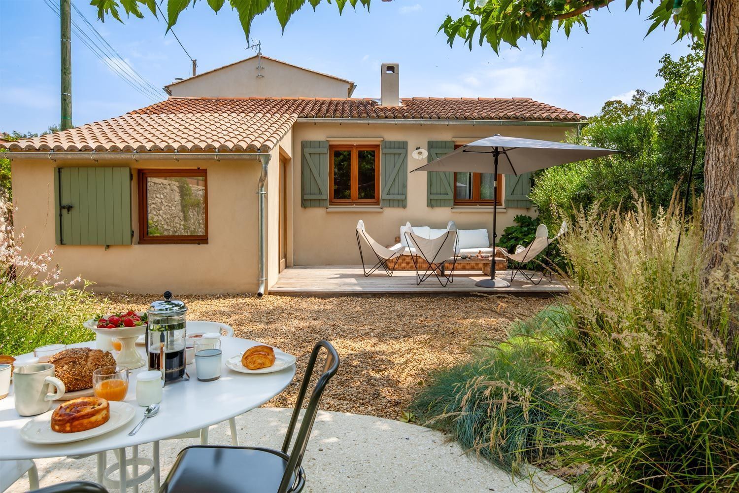 Ein Haus mit Ziegeldach, einer Terrasse mit Gartenmöbeln und einem Tisch, gedeckt mit Frühstücksleckereien.