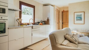 Una cucina moderna con mobili bianchi, stipite in legno e zona pranzo con divano beige.