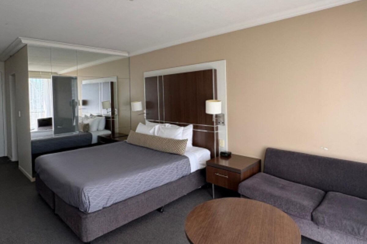 Ein Hotelzimmer mit einem großen Bett, einem Schlafsofa, einem kleinen Tisch, einem Spiegel und einem Kleiderschrank.