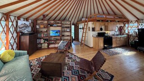 Ruim yurt interieur met dakkoepel, televisie, houten meubels en een keukenhoek.