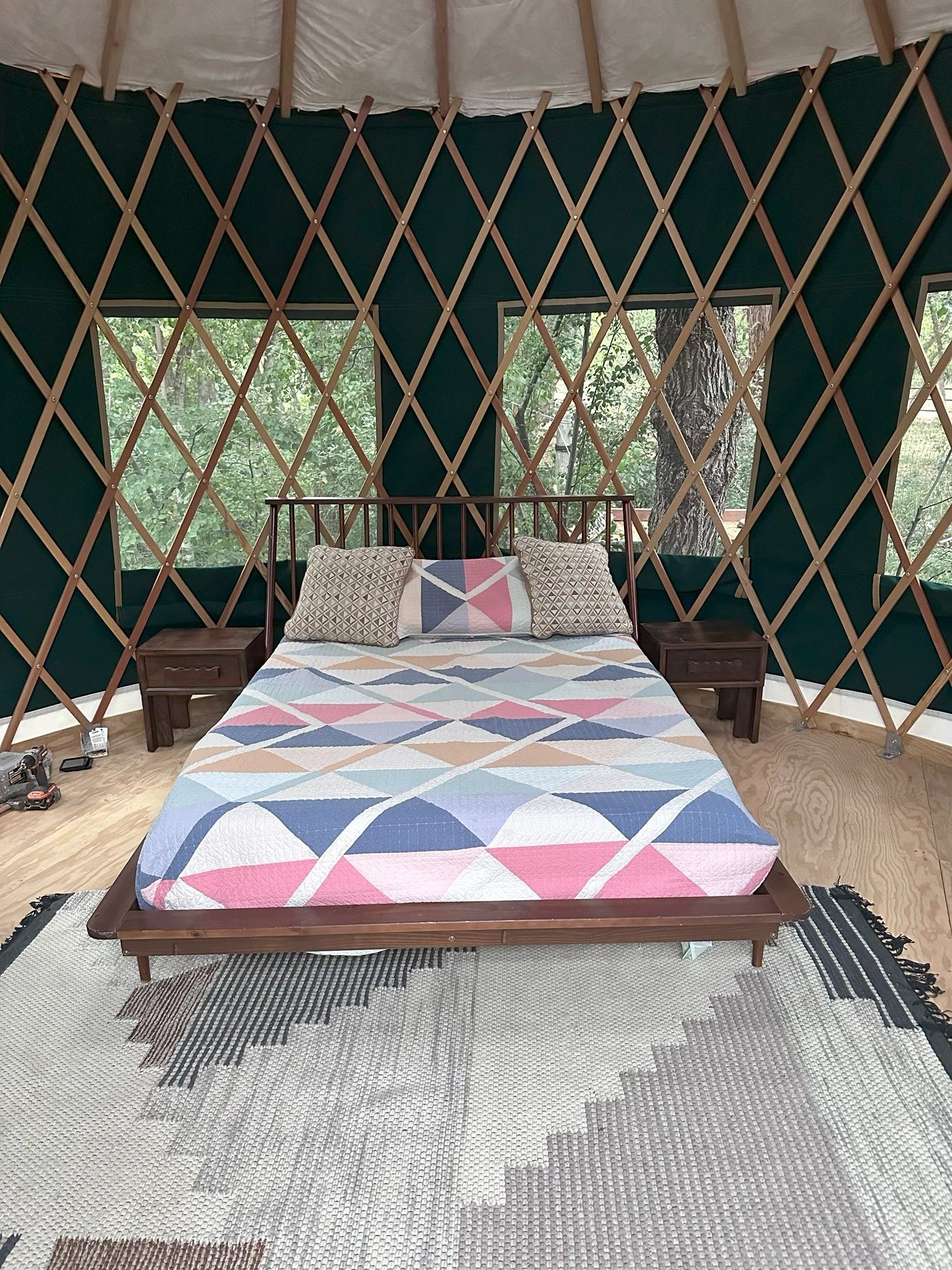 A bed with a geometric patterned bedspread, two bedside tables, and a view of trees through a lattice window.
