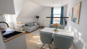A compact living space with a kitchenette, a dining area with two chairs, a sofa, and a small table with a vase. - Modern, central apartment for up to 4 people right next to the old lighthouse (Borkum)
