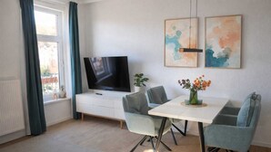 A modern living room with a flat-screen TV, a dining table with chairs, and two abstract paintings on the wall. - Modern, central apartment for up to 4 people right next to the old lighthouse (Borkum)