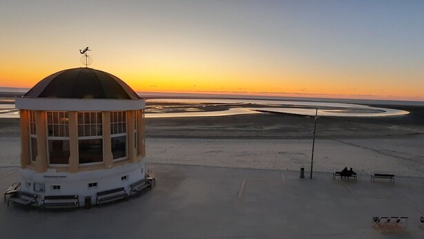 A building with a dome and a weather vane, surrounded by a sandy area with benches and a clear sky. - Modern, central apartment for up to 4 people right next to the old lighthouse (Borkum)