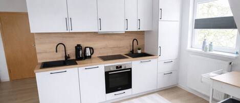 A modern kitchen with white cabinets, a double sink, a built-in oven, and a window with a view.