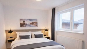 A bedroom with a bed, bedside lamps, a window with a view, a radiator, and a ceiling light. - Modern, central apartment for up to 4 people right next to the old lighthouse (Borkum)