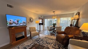 Una sala de estar con televisión, chimenea, comedor y cocina al fondo.
