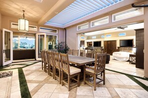 Un vaste espace dédié à la salle à manger, avec une grande table et des chaises en bois, un ventilateur de plafond et une vue sur l’extérieur.