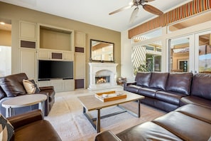 A living room with a fireplace, leather sofas, a flat-screen TV, and a ceiling fan.