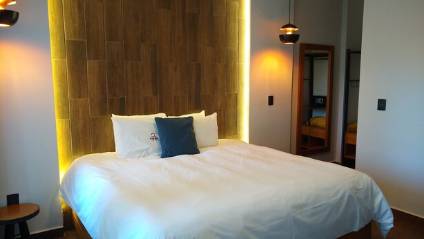 A neatly made bed with white bedding and a blue pillow, a wooden headboard, and two pendant lights. - HOTEL CONSTITUCION (Mineral del Monte)