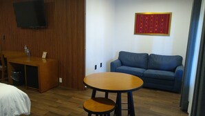 A room with a wooden desk, a blue sofa, a round table, and a mounted TV. - HOTEL CONSTITUCION (Mineral del Monte)