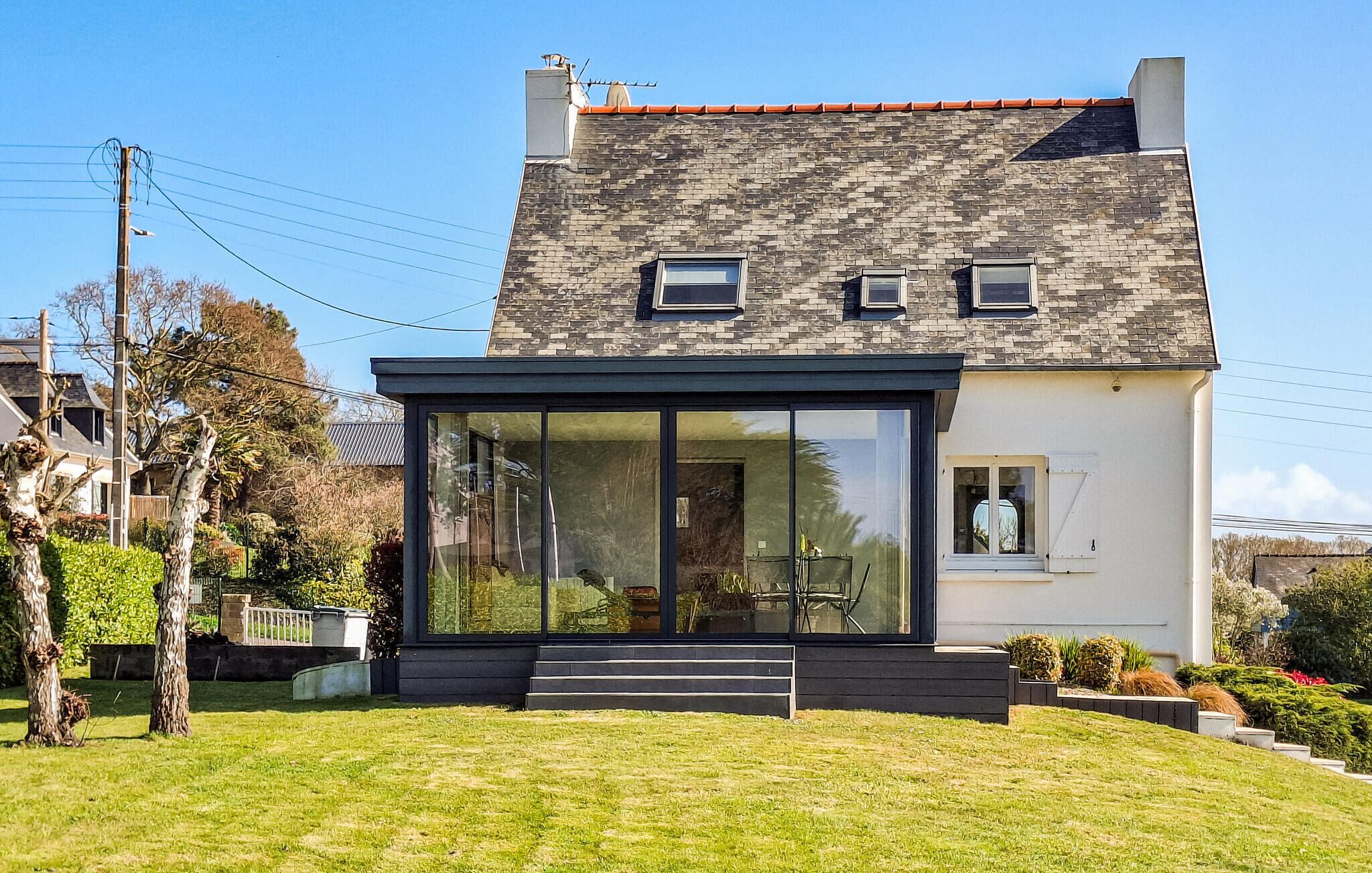 Una casa moderna de dos pisos con un amplio ventanal, una chimenea y un pequeño balcón.
