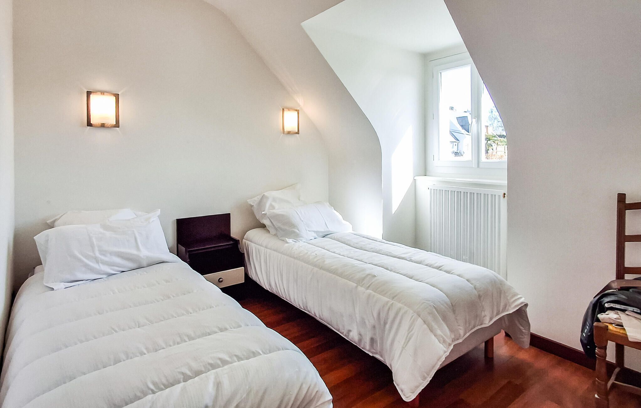 A bedroom with two beds, a nightstand, a dresser, and a window with a view.