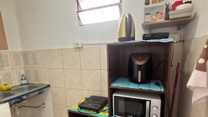 A compact kitchen with a microwave, kettle, and a small shelf with a poster.