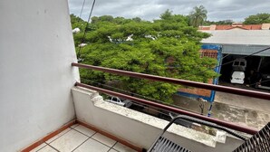 A balcony with tiled flooring, a metal chair, and a view of trees and buildings.