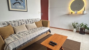 A living room with a sofa, a coffee table, a wall-mounted shelf with plants, a door, and a framed picture.