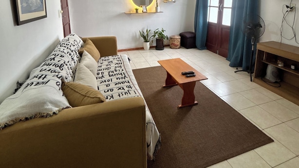 A living room with a sofa, a coffee table, a ceiling fan, a TV, and a window with curtains.