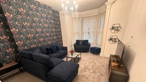Ein Wohnzimmer mit Ecksofa, Hocker, Couchtisch und einem TV-Schrank.