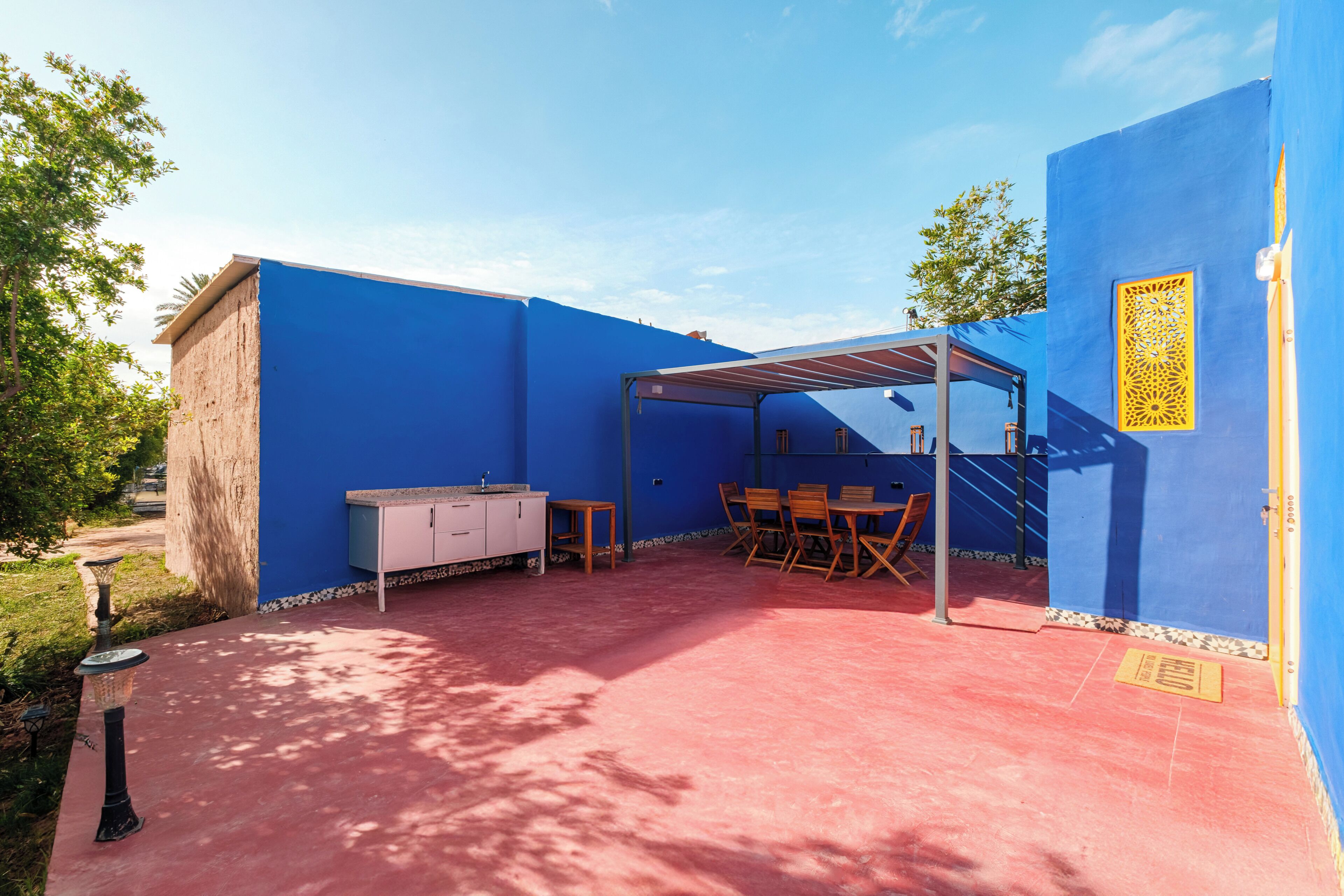 A covered outdoor seating area with a table and chairs, a small cabinet, and a decorative wall panel.