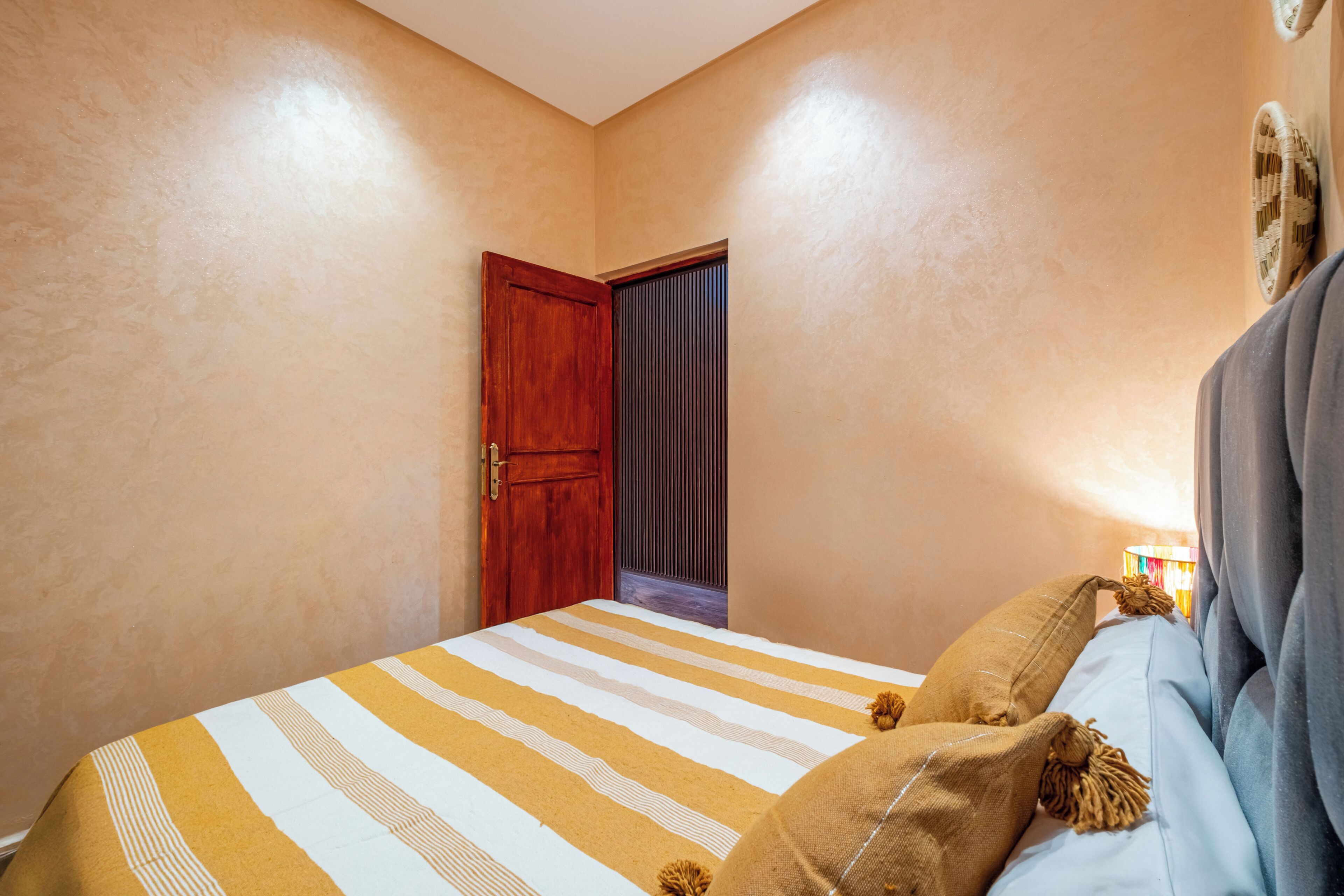 A bedroom with a bed, a wooden door, and a wall-mounted lamp.