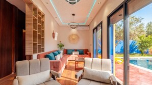 Una sala de estar moderna con un sofá, sillas, una mesa de centro y un ventanal con vista a una piscina.