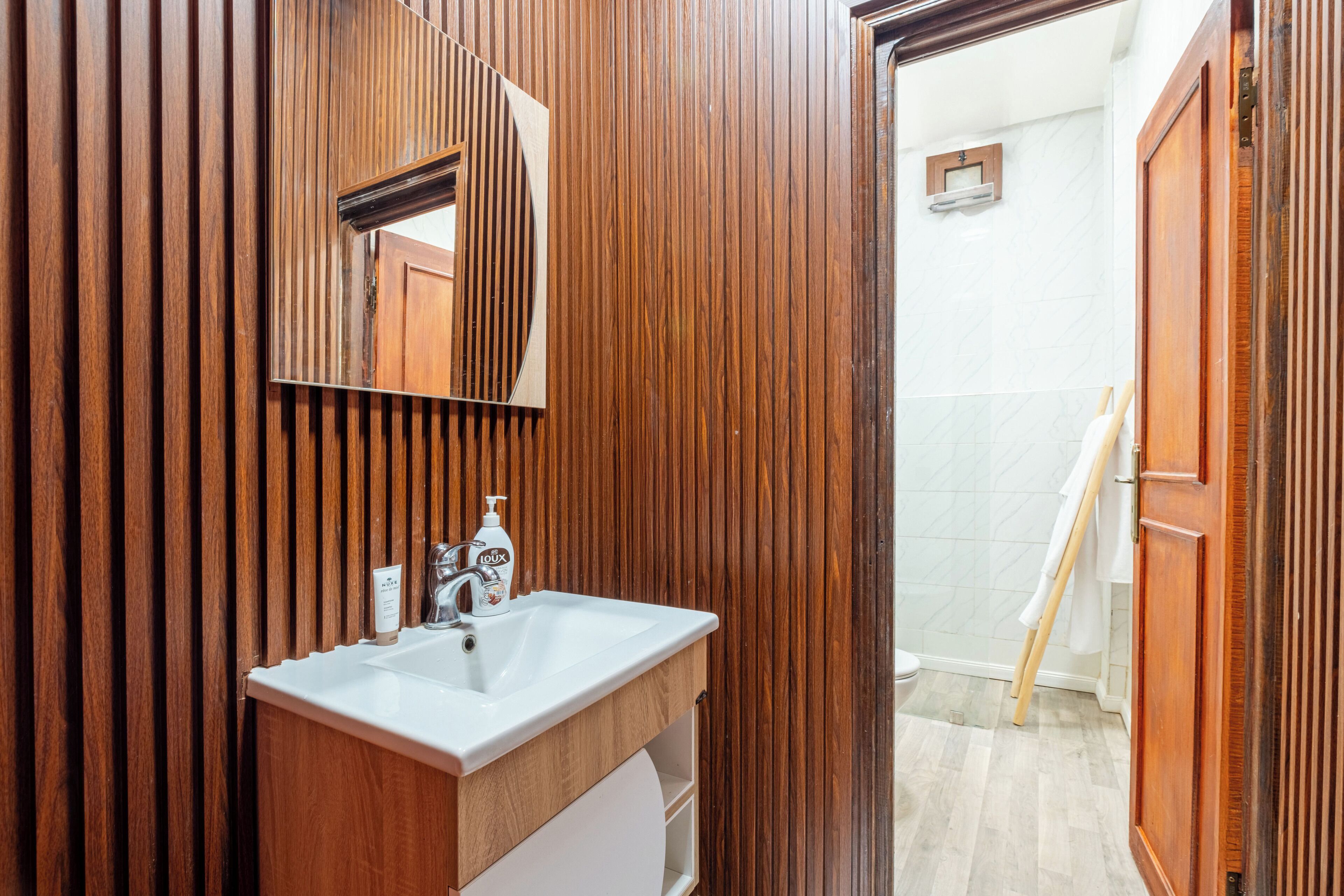 A bathroom with a wooden vanity, a sink, a mirror, and a towel rack.