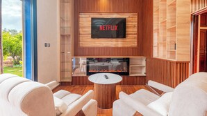 Una sala de estar moderna con chimenea, un televisor montado en la pared y vistas al exterior.
