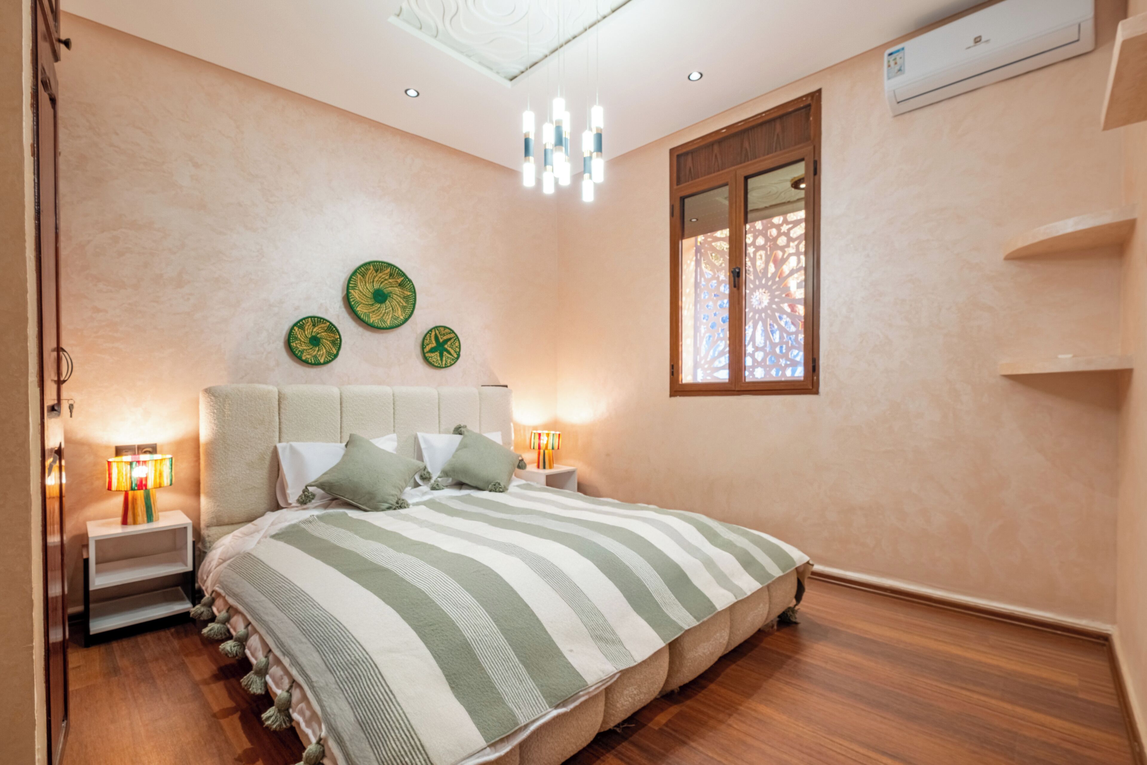 A bedroom with a large bed, bedside lamps, decorative plates on the wall, and a window with a patterned view.