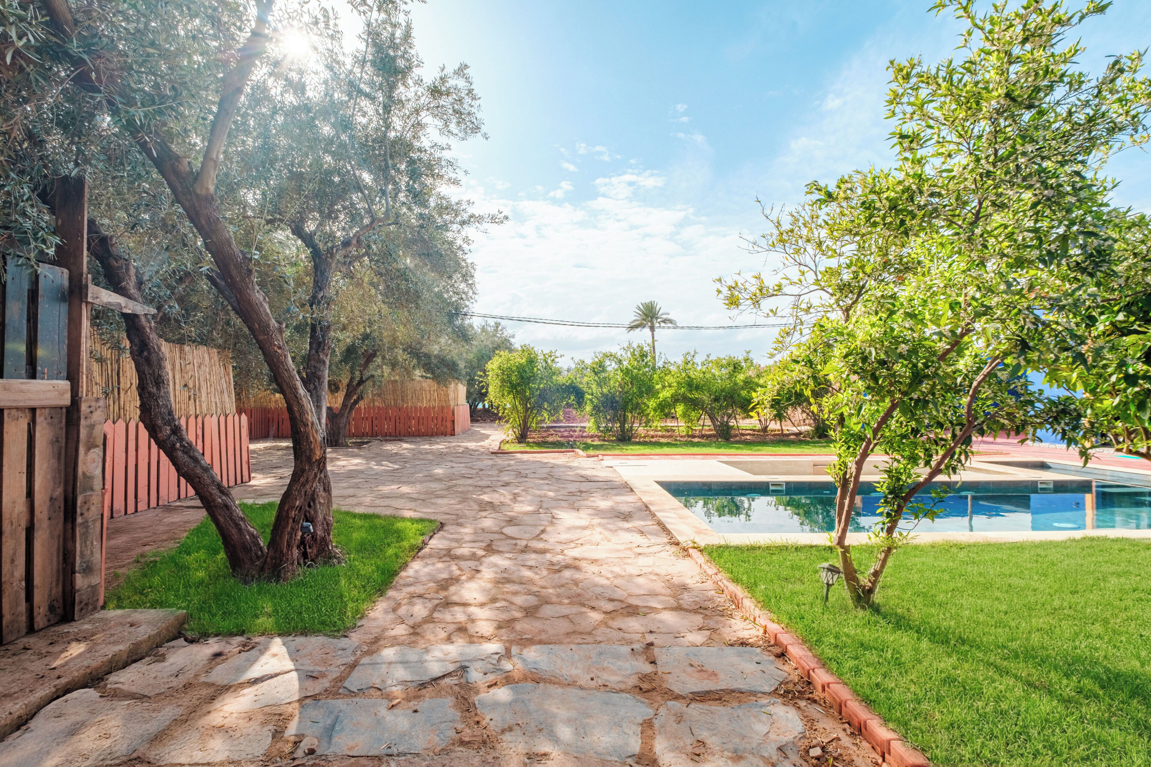 Un sendero de piedra que lleva a una piscina, rodeada de follaje y una valla de madera.