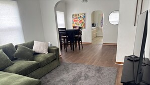 A living room with a green sofa, a grey rug, a TV, and a dining area with chairs and a table. - Close to West Valley Hospital and Golf course in Caldwell, ID (Caldwell)