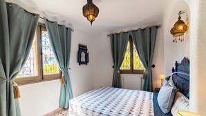 Ein Schlafzimmer mit Bett, Vorhängen, einer Wandlampe und einem gemusterten Boden.