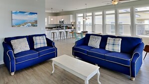 Een woonkamer met twee blauwe banken, een witte salontafel en een keuken op de achtergrond.