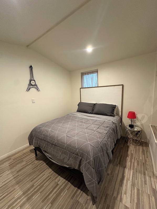 A bedroom with a bed, a red lamp, a wall clock, and a window with curtains.