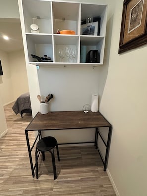 A dining area with a wooden table, black chairs, a white shelf with kitchenware, and a framed picture on the wall.
