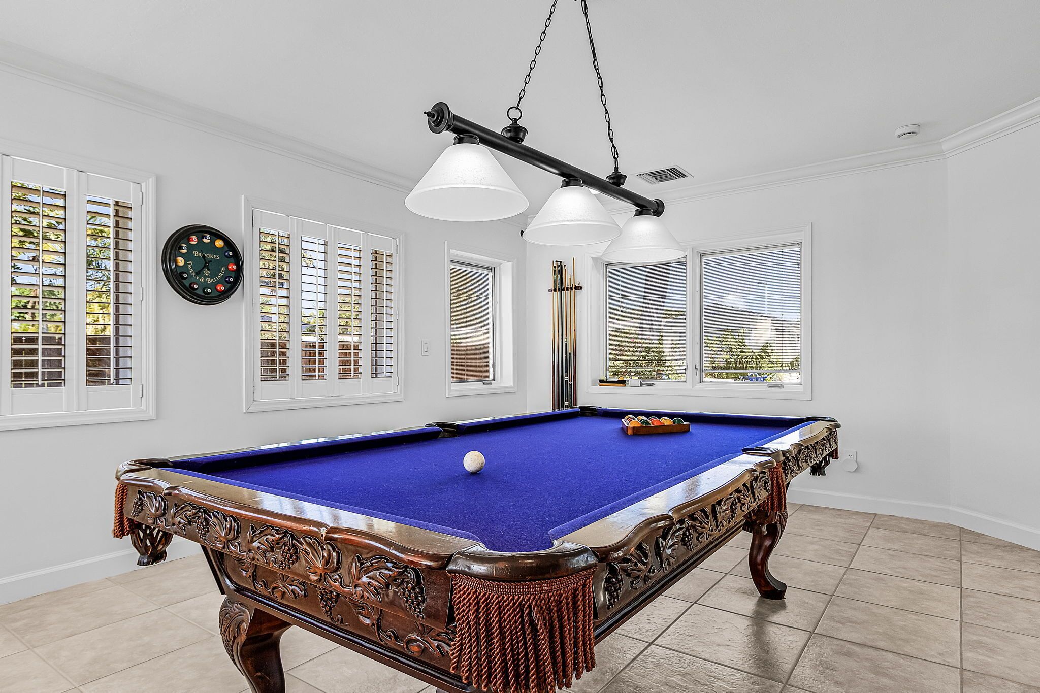 A pool table with a blue felt surface, surrounded by white walls and windows with blinds.