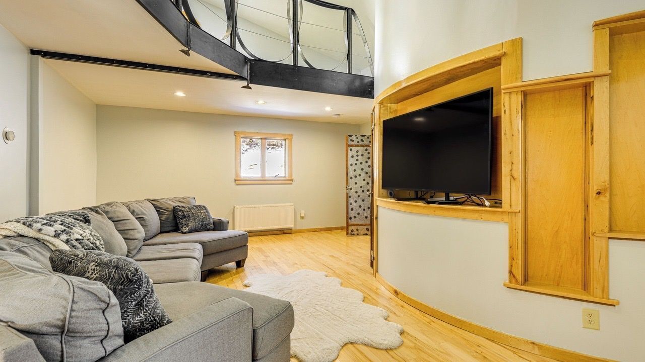 Een moderne woonkamer met een modulaire bank, een flatscreen televisie bevestigd aan een houten wand, een trap en een groot raam.