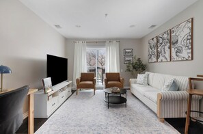 A living room with a television, two armchairs, a sofa, a coffee table, and artwork on the wall.