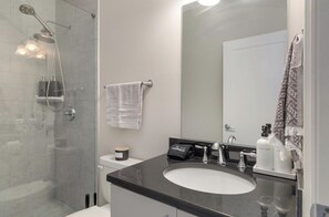 A modern bathroom with a glass-enclosed shower, a white toilet, a black sink with a mirror above it, and toiletries on the countertop.
