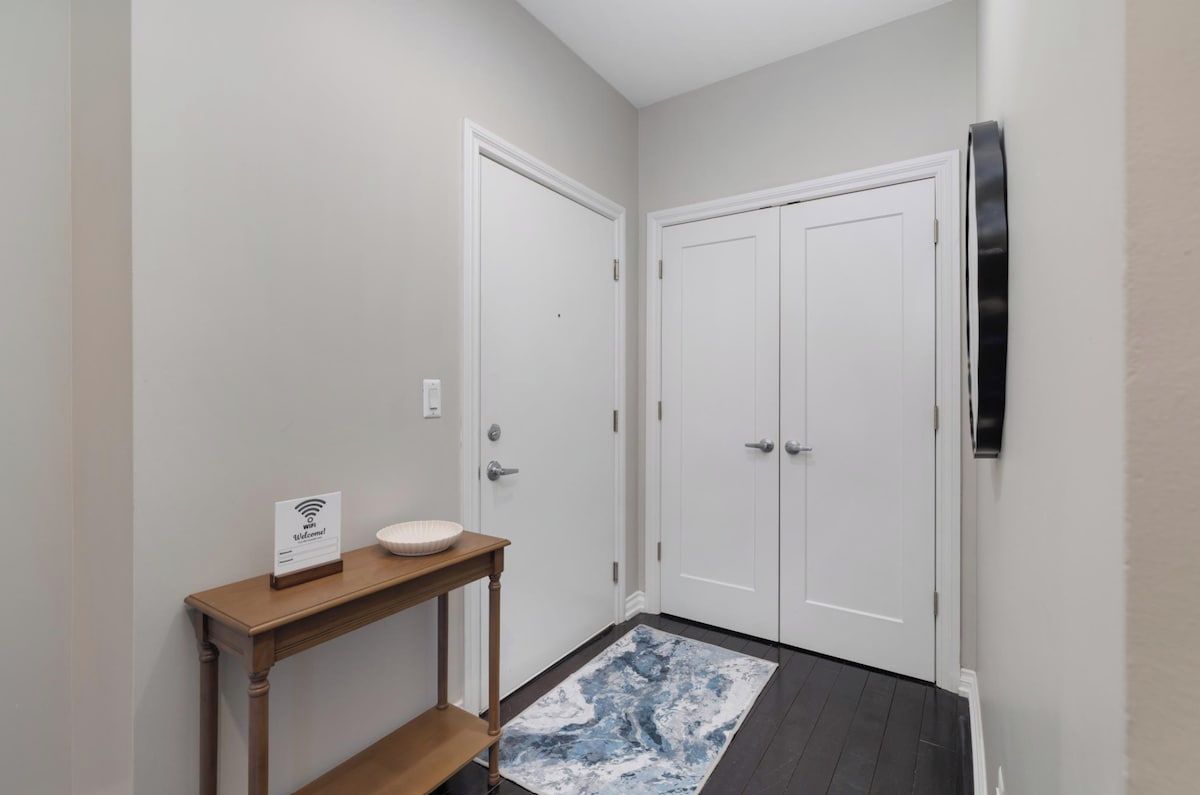 Un couloir avec deux portes blanches, une console en bois surmontée d’un lavabo blanc, et un tapis aux motifs bleus et blancs.