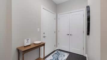 Un couloir avec deux portes blanches, une console en bois surmontée d’un lavabo blanc, et un tapis aux motifs bleus et blancs.