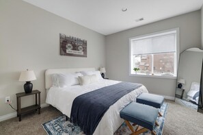 A bedroom with a bed, bedside tables, a window with blinds, and a mirror.