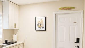 A kitchen with white cabinets, a bench, a door, and a framed picture on the wall. - Paradiso Shores (Miami)
