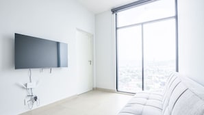 Una habitación moderna con un ventanal grande, un televisor de pantalla plana en la pared y un sofá de color claro.
