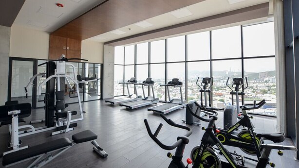 Un gimnasio con máquinas de cardio, equipo de pesas y un amplio ventanal con vista a la ciudad.