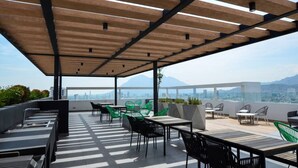 Terraza en la azotea con mobiliario exterior, una pérgola y vistas panorámicas de la ciudad.