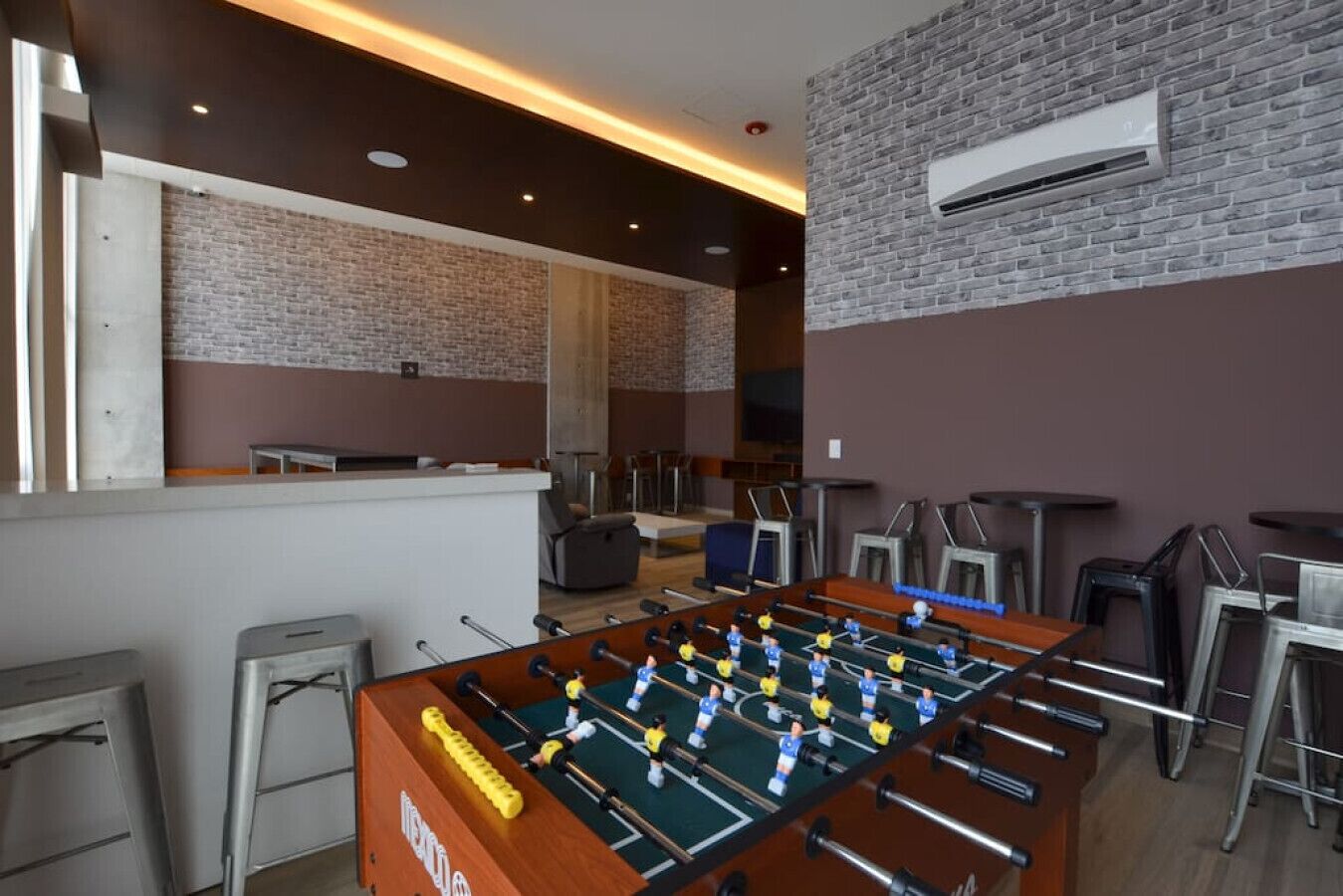 Un tavolo da calcio, sgabelli da bar e una parete in mattoni.