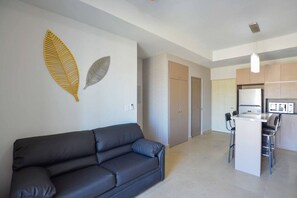 Un salon moderne avec un canapé, un coin cuisine comprenant une table et des chaises, et un couloir menant à une porte.