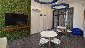 A conference room with a flat-screen TV, round tables, and chairs, surrounded by a green wall and a glass partition. - Obra de Arte y un Increíble, Amplio Departamento (Monterrey)